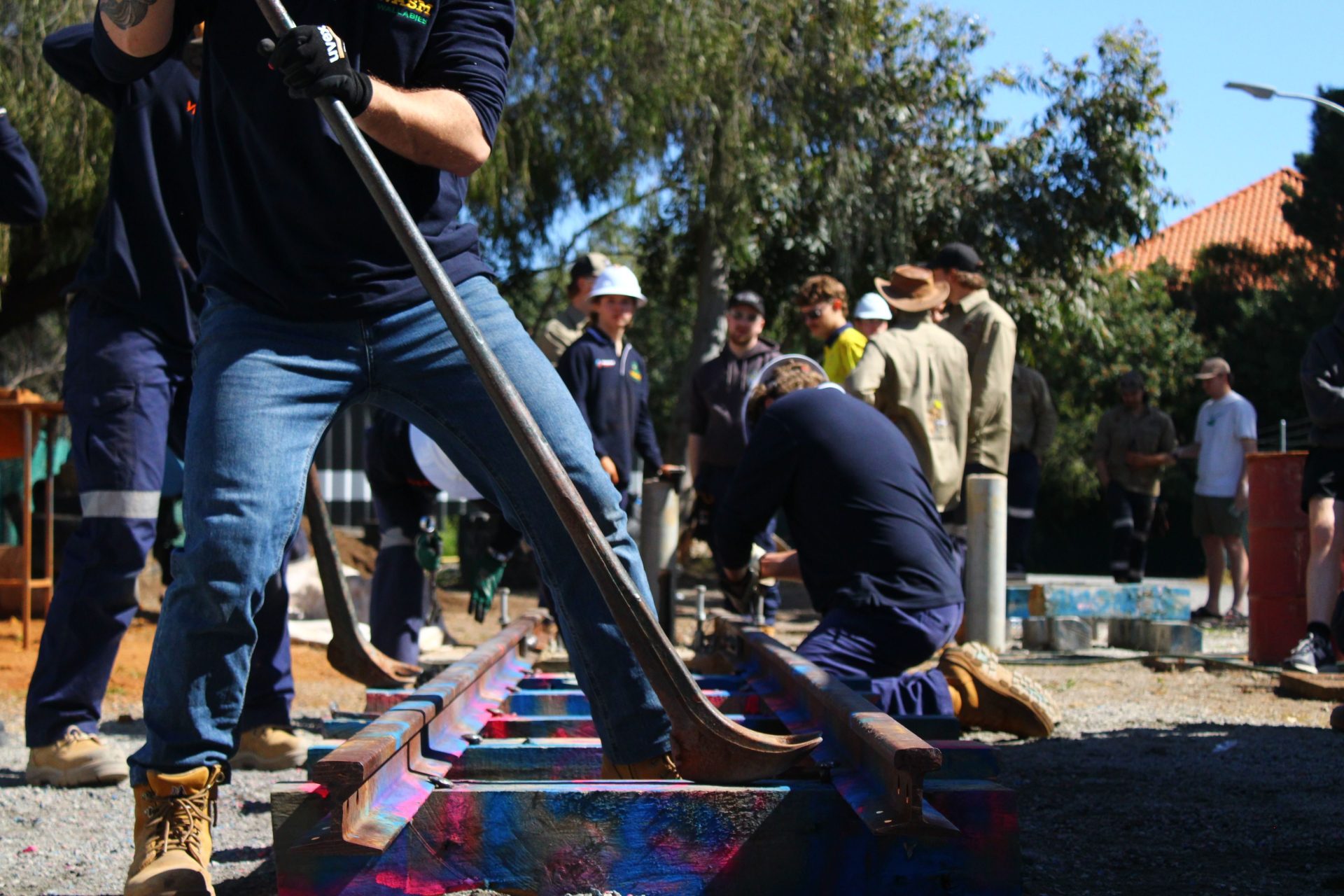 Eine Gruppe von Erwachsenen bei einer Veranstaltung zum Bau einer Eisenbahnstrecke im Freien, bei der die Teamfähigkeit gefördert wird.